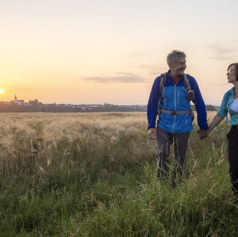 Ein Paar wandert bei Sonnenuntergang durch ein Feld. Im Hintergrund ist eine Stadt zu sehen., © Kappest_REMET Ein Paar wandert bei Sonnenuntergang durch ein Feld. Im Hintergrund ist eine Stadt zu sehen., © Kappest_REMET