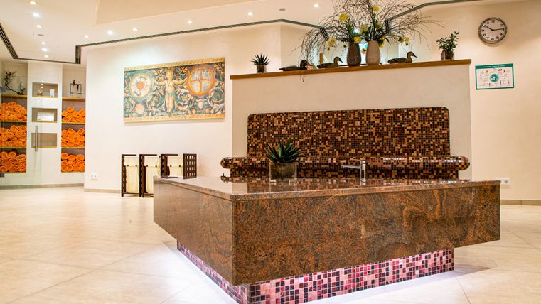 An elegant reception area with a decorative marble table. The walls are adorned with plants and artworks that create an inviting atmosphere.