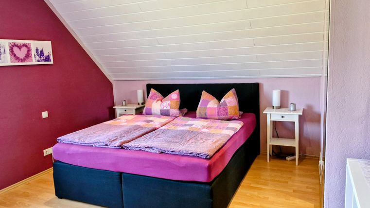 Ein gemütliches Schlafzimmer mit einem großen Bett und bunten Kissen. Die Wände sind in sanften Farben gestrichen und es gibt kleine Nachttische daneben.