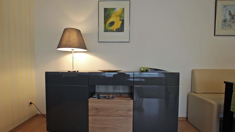 Ein moderner Wohnzimmertisch aus Holz und Glas steht an einer Wand. Über dem Tisch hängen zwei Bilder und eine Lampe beleuchtet den Raum.