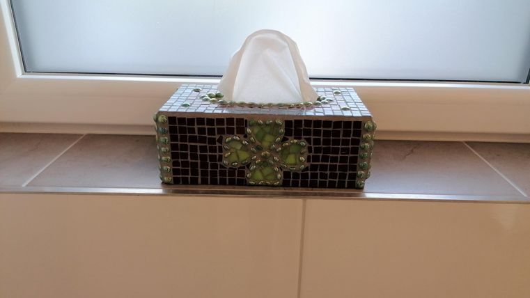 A decorative tissue box with a green pattern is on a windowsill. The light shines through the window and illuminates the box.