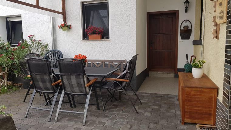 A cozy courtyard with a table and chairs. Next to the entrance door are plants and a wooden chest of drawers.