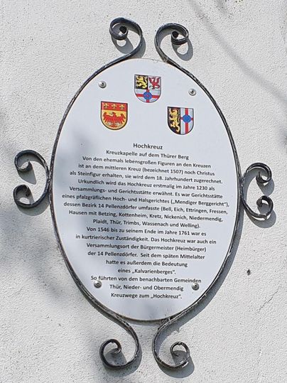 Eine informierende Tafel mit historischen Informationen und Wappen. Sie befindet sich an einer Wand und beschreibt die Bedeutung des Ortes "Hochkreuz".