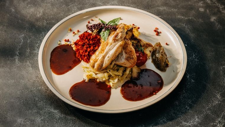 Ein kunstvoll angerichteter Teller mit gegrilltem Hähnchen, pürierten Kartoffeln und verschiedenen Saucen. Eine farbenfrohe Beilage aus Paprika und Kräutern ergänzt das Gericht.