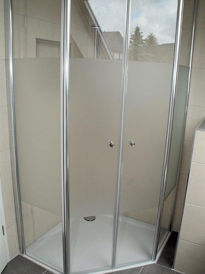 Eine moderne Duschkabine mit transparenten und matten Glastüren. Der Boden ist fließen ausgelegt und bietet einen eleganten Look.