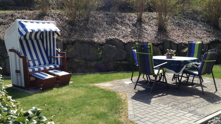 A cozy garden with a beach chair and a table with chairs. Green spaces and a little shade create an inviting atmosphere.