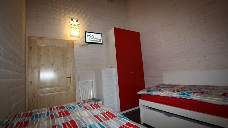 Ein gemütliches Zimmer mit zwei Betten und bunten Bettdecken. An der Wand befindet sich ein Fernseher und ein roter Schrank.