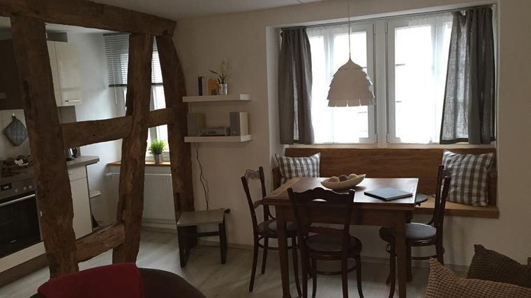 Ein gemütlicher Essbereich mit einem Holzstamm und einem Tisch, umgeben von Stühlen. Große Fenster sorgen für viel Tageslicht.