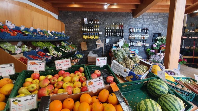 A colorful fruit and vegetable stand in a store. Fresh products are neatly arranged, including apples, melons, and pineapples.