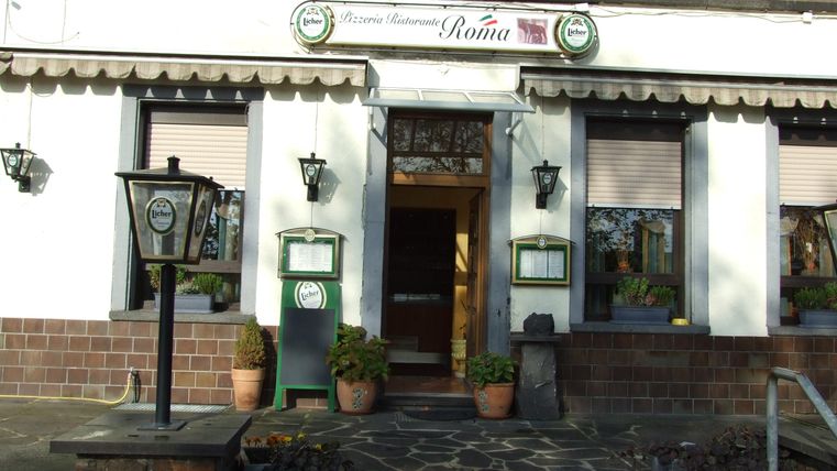 Das Bild zeigt den Eingangsbereich eines Restaurants mit einem einladenden Ambiente. Es gibt Pflanzen und eine Steintreppe, die zu einem stilvollen Eingangsbereich führt.