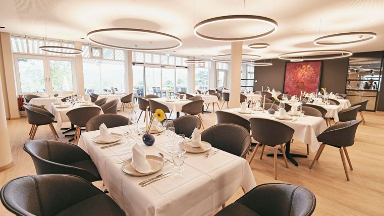 An elegant restaurant with round tables and modern furnishings. Large windows provide ample daylight and a welcoming atmosphere.
