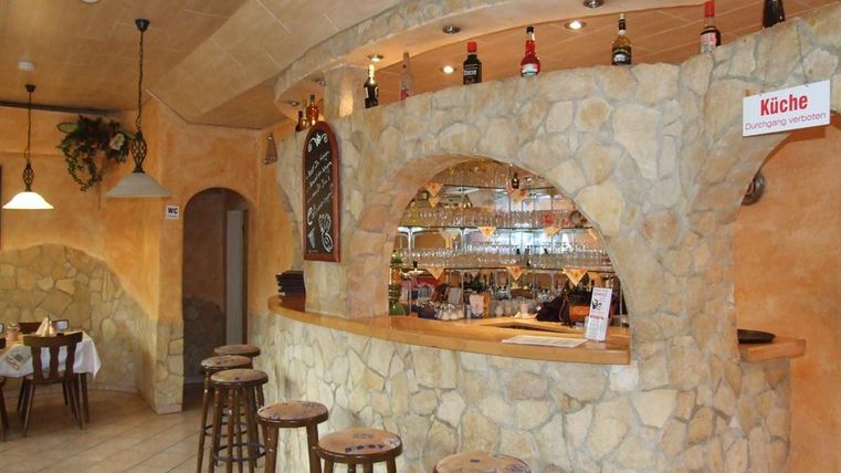 An inviting bar with a stone counter and barrels. The walls are in warm colors and there are tables in the background.