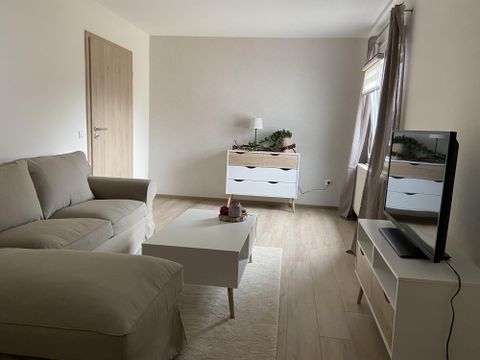 A bright living room with a beige sofa and a white coffee table. Opposite is a television on a modern sideboard.
