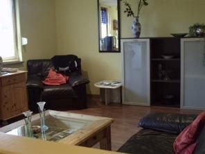 A cozy living room with a black sofa and a wooden table. On the wall, there is a vase and a mirror, the room has warm yellow walls.