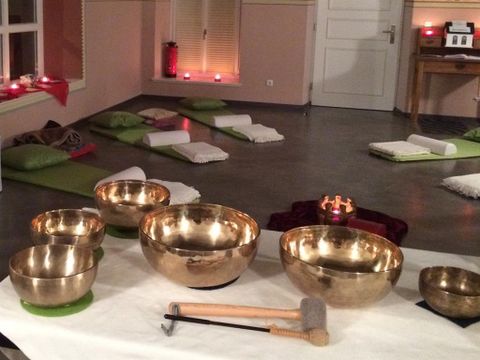 Ein meditativer Raum mit mehreren Klangschalen auf einem Tisch. Im Hintergrund liegen Matten und sanfte Beleuchtung sorgt für eine entspannte Atmosphäre.