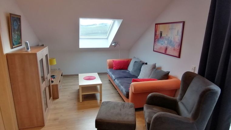 A bright, modern living room with a cozy sofa and an armchair. The skylight provides plenty of daylight.