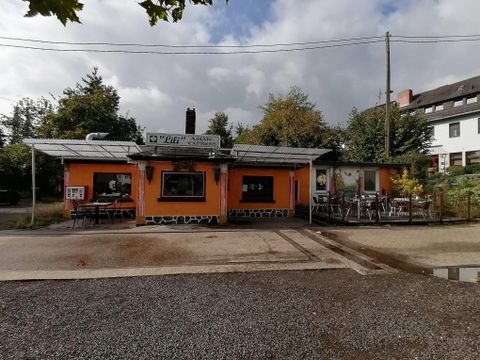 A cozy restaurant with an orange facade and outdoor tables. Surrounded by trees and a quiet street.