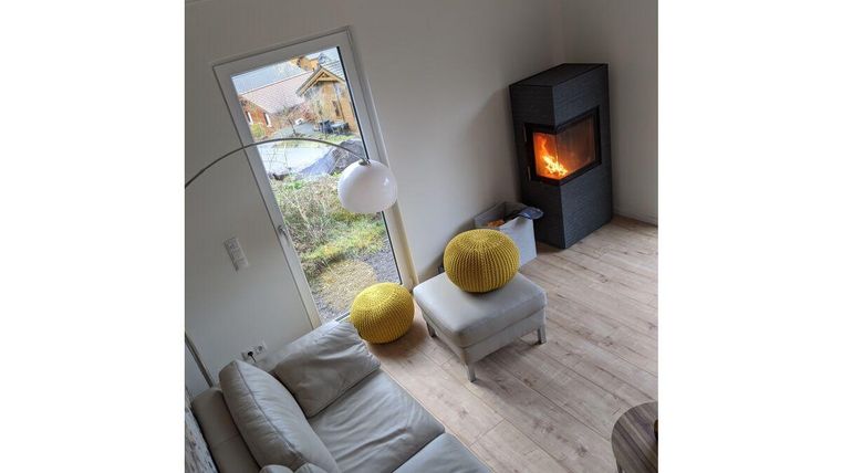 Ein modernes Wohnzimmer mit einem hellen Sofa und einem gemütlichen Kamin. Durch das Fenster sieht man die Natur draußen.