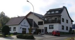 Ein charmantes zweigeschossiges Gebäude mit einem Balkon und einer Terrasse. Vor dem Haus steht ein rotes Auto und es gibt einen Parkplatz.