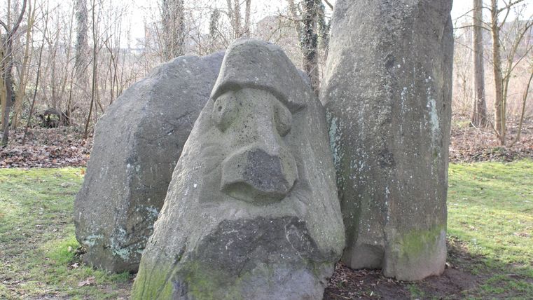Drei große, beieinanderstehende Steine, davon ein Stein mit einem eingekerbten Gesicht versehen