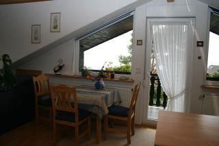 Ein gemütlicher Essbereich mit einem Tisch und Stühlen. Durch eine gläserne Tür ist ein Balkon mit Blick ins Freie zu sehen.