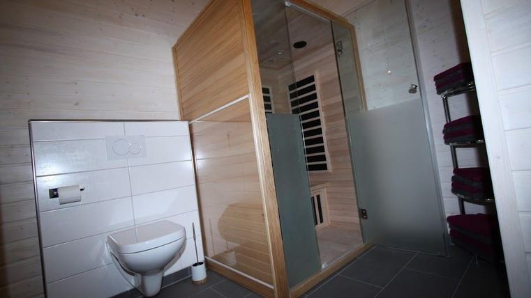 Ein modernes Badezimmer mit einer Dusche und einer Sauna aus Holz. Die Wände sind hell und der Boden ist mit Fliesen ausgestattet.