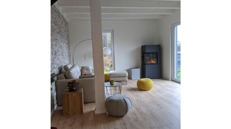 Ein modernes Wohnzimmer mit einem gemütlichen Sofa und einem Kamin. Helle Wände und viel Licht sorgen für eine einladende Atmosphäre.
