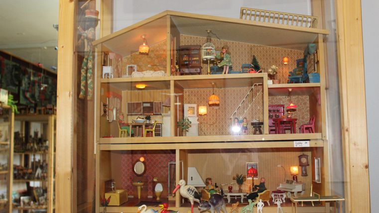 Ein liebevoll gestaltetes Puppenhaus mit mehreren Zimmern und vielen Spielzeugfiguren. Es zeigt einen warmen und einladenden Innenraum mit verschiedenen Möbeln und Details.