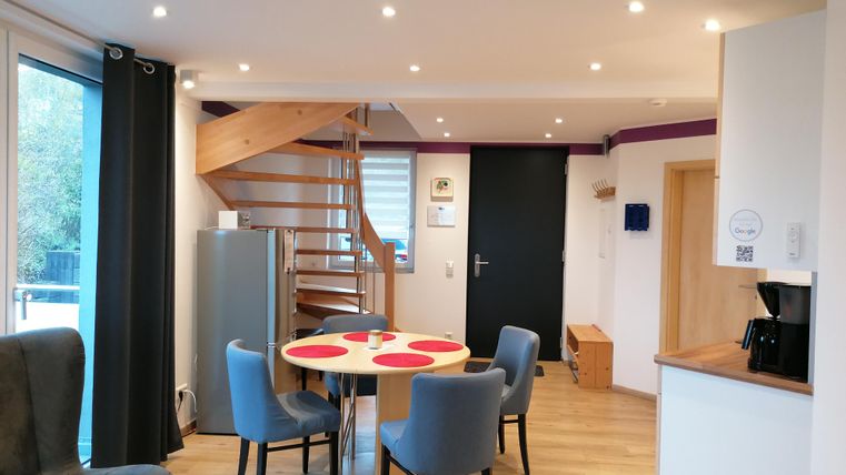 A modern apartment with a cozy seating area and a dining area. The wooden staircase leads to an upper area.