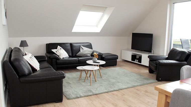 Ein modernes Wohnzimmer mit schwarzen Sofas und einem flachen Fernseher. Ein Teppich und ein kleiner Tisch runden die gemütliche Atmosphäre ab.