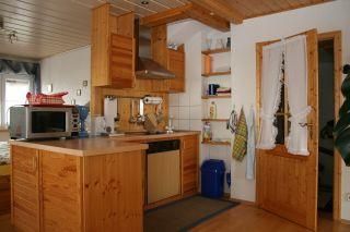 Eine moderne Küche mit Holzschränken und einem offenen Raumkonzept. Es gibt eine Spüle, einen Herd und verschiedene Küchengeräte.