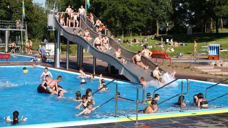 Ein beliebtes Freibad mit vielen Menschen, die im Wasser spielen. Rutschen und Sonnenschirme sind ebenfalls sichtbar.