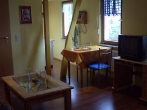 A cozy room with a table, chairs, and a television. The walls are painted yellow, and there are large windows that let in daylight.