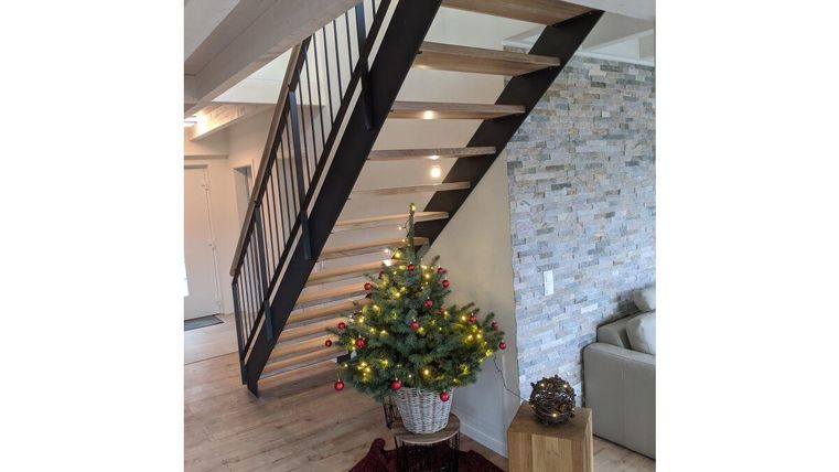 Eine moderne Treppe aus Holz und Metall führt nach oben. Vor der Treppe steht ein geschmückter Weihnachtsbaum in einem Korb.