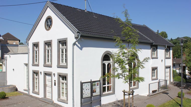 Ein modernes, weißes Gebäude mit einem klaren Himmel im Hintergrund. Es hat große Fenster und einen eleganten Eingang.