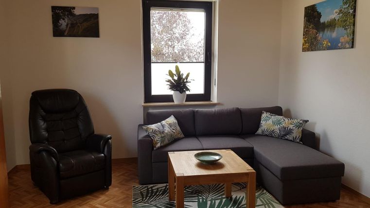 A cozy living room with a gray sofa and a black leather armchair. On the table is a bowl, and in the background there are plants and pictures on the wall.