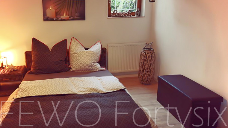 A cozy bedroom with a large bed and decorative cushions. The window brings natural light and a relaxing atmosphere.