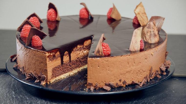 A delicious chocolate cake with raspberries and chocolate chips. The cake has multiple layers and a shiny sugar glaze.