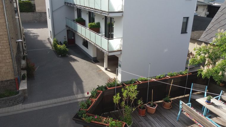 Ein modernes Wohngebäude mit Balkonen und Pflanzen entlang der Fassade. Im Vordergrund sind Gartenpflanzen und eine Terrasse zu sehen.