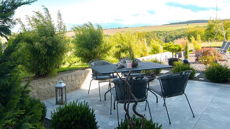 Ein schöner Gartenbereich mit einem Tisch und Stühlen auf einer Terrasse. Üppige Pflanzen umgeben den Platz und bieten eine entspannende Atmosphäre.