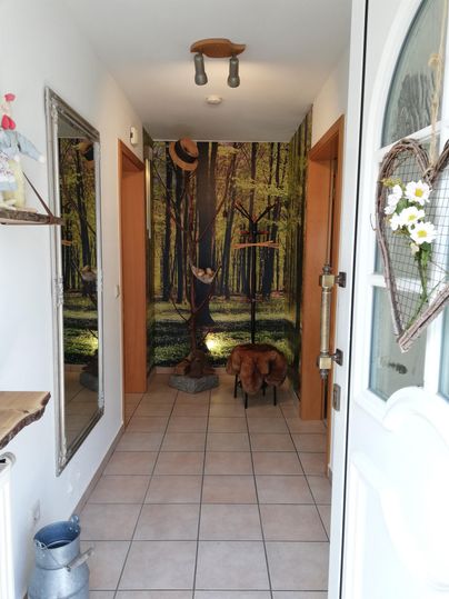 An inviting hallway with a forest motif on the wall. The room is bright and has tiled flooring with a cozy stool.