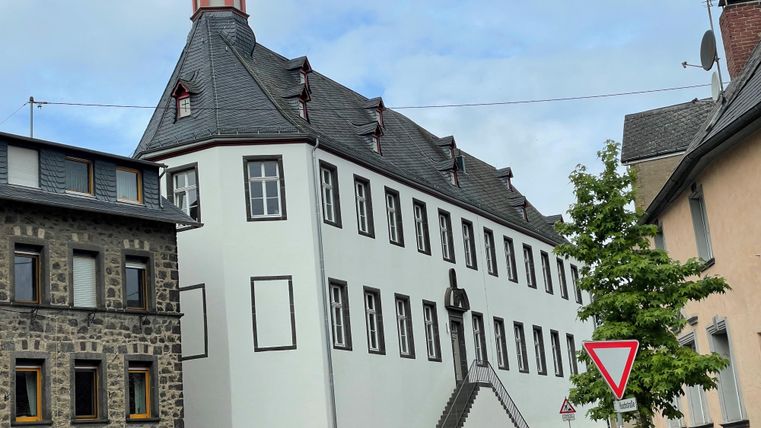 Ein historisches Gebäude mit einem markanten Turm und einer Wetterfahne. Der Himmel ist klar und blau.