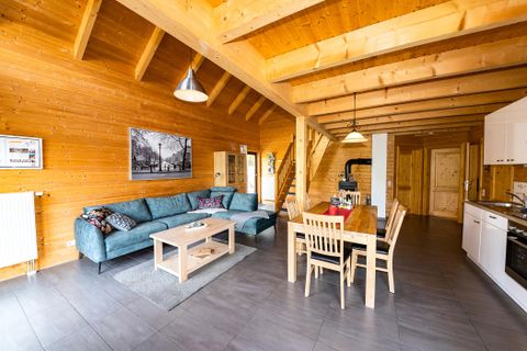 Ein gemütlicher Wohnbereich in einem Holzhaus mit Sofa und Esstisch. Die Holzdecke und Wände schaffen eine warme Atmosphäre.