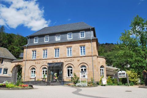 A historical building with an elegant facade and a bright sky. In the foreground, flowers and trees can be seen.