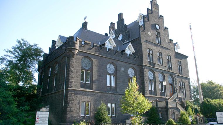 Ein historisches Gebäude mit einer beeindruckenden Fassade aus dunklem Stein. Das Gebäude hat viele Fenster und beeindruckende architektonische Details.