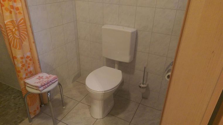 A simple bathroom with a toilet and a shower. A chair and towels are also available.