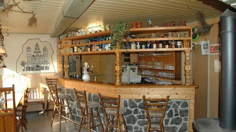 Eine gemütliche Bar mit Holzvertäfelung und einer Auswahl an Spirituosen. Helle Beleuchtung und rustikale Stühle schaffen eine einladende Atmosphäre.