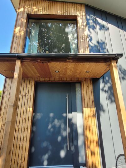 Ein modernes Haus mit einer Holzverkleidung und einer großen Glastür. Die Eingangstür ist elegant und minimalistisch gestaltet.