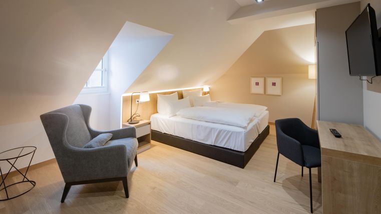 Ein modernes Schlafzimmer mit einem großen Bett und gemütlichen Möbeln. Die Wände sind hell und der Raum hat ein helles, einladendes Ambiente.