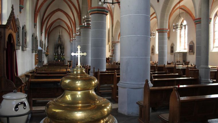 A historic church with wooden benches and high, vaulted ceilings. In the middle stands a golden baptismal font.
